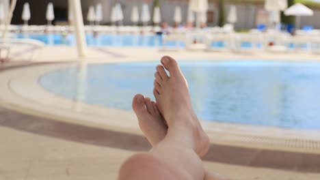 Men's-feet-on-the-background-of-the-swimming-pool,-relax-on-vacation