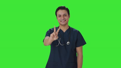 Fröhlicher-Indischer-Arzt-Zeigt-Siegeszeichen-Auf-Grünem-Bildschirm