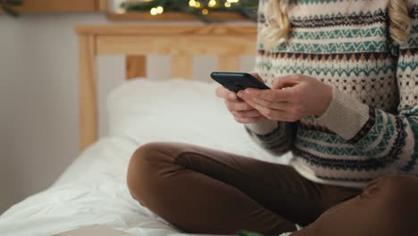 Unrecognizable-woman-using-phone-while-sitting-on-Christmas-time.