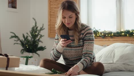 Kaukasische-Frau-Sitzt-Auf-Dem-Bett-Und-Fotografiert-Mit-Dem-Smartphone-Verpackte-Weihnachtsgeschenke
