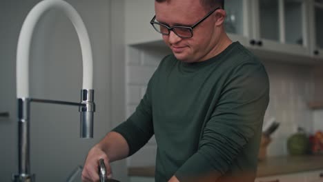 Tilt-up-of-adult-caucasian-man-with-down-syndrome-washing-dishes-at-home.