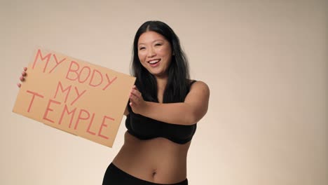Smiling-plus-size-woman-in-black-underwear-dancing-in-the-studio-and-holding-a-banner.