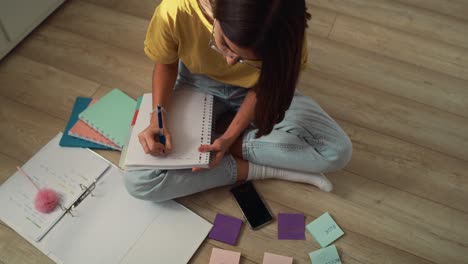Kaukasisches-Teenager-Mädchen-Sitzt-Auf-Dem-Boden-Und-Lernt-Aus-Karteikarten-Und-Einem-Notizbuch