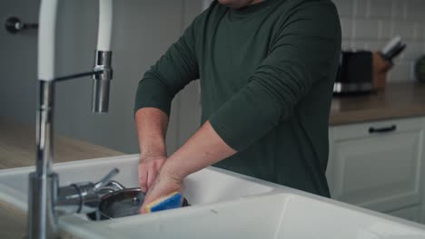 Tracking-video-of-adult-caucasian-man-with-down-syndrome-washing-dishes-at-home.
