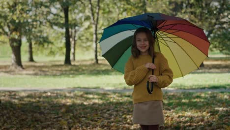 Little-girl-standing-at-the-park-with-colorful-umbrella-during-the-autumn.