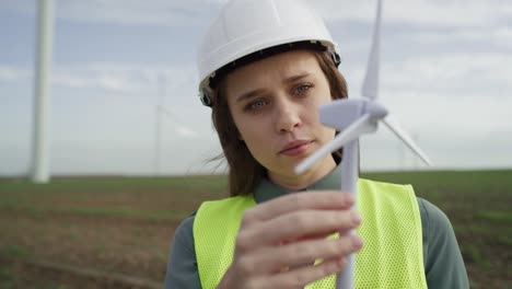 Female-caucasian-engineer-standing-outdoors-and-checking-wind-turbine-field-plastic-model.