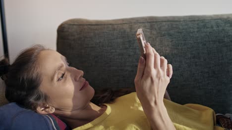 Caucasian-woman-lying-on-sofa-and-browsing-phone