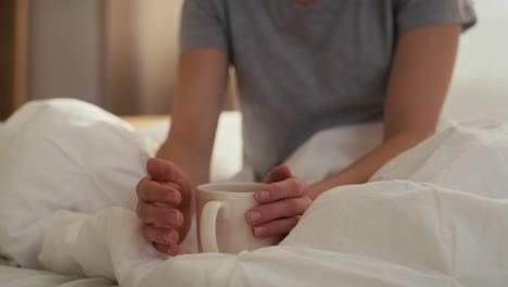 Close-up-of-cup-of-coffee-in-woman's-hand-in-the-bed-at-morning