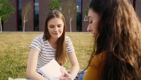Two-female-caucasian-students-studying-outside-the-university-campus.