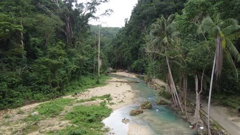 Mujeres-Filipinas-Lavando-Ropa-Y-Nadando-En-El-Agua-Azul-Del-Arroyo-En-Medio-De-Una-Exuberante-Jungla-De-Cañones-En-Badian,-Cebú