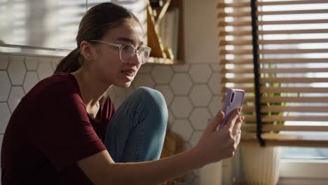 Kaukasisches-Teenager-Mädchen,-Das-In-Der-Küche-Sitzt-Und-Einen-Videoanruf-Auf-Dem-Mobiltelefon-Führt