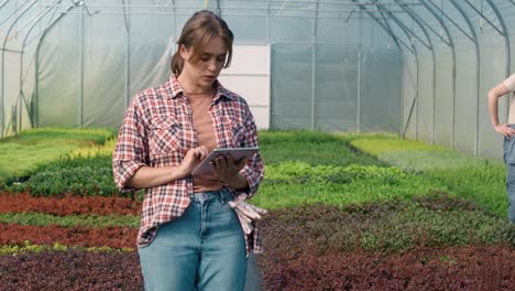 Caucasian-female-botanist-standing-in-the-greenhouse-and-using-digital-table