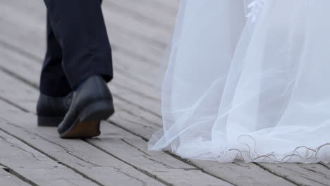 A-man-in-a-black-suit-and-shoes-is-walking-on-the-pier-beside-his-bride-to-be