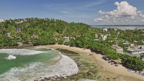Mirissa-Sri-Lanka-Aerial-v18-cinematic-drone-flyover-bay-capturing-beautiful-golden-sandy-beach,-hillside-beachfront-resort-hotels-and-blue-ocean-views---Shot-with-Mavic-3-Cine---April-2023