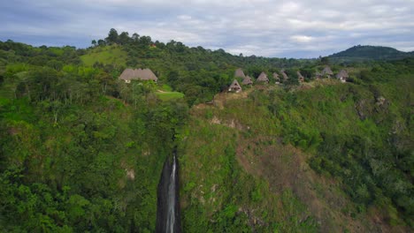 Thatched-roof-bungalows-hotel-on-tropical-jungle-with-waterfall-on-top-of-canyon