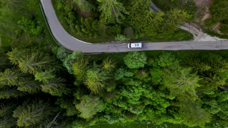 A-camper-van-drives-quickly-down-a-forest-road,-the-camera-tracks-from-above
