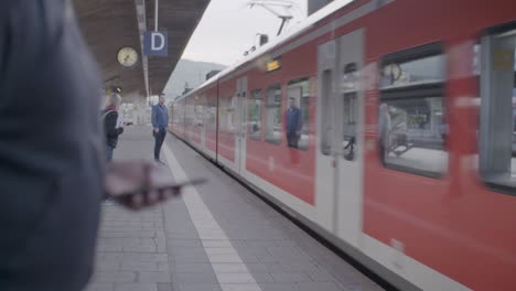 High-speed-electric-passenger-train-arriving-at-station-while-passenger-looks-at-his-smartphone