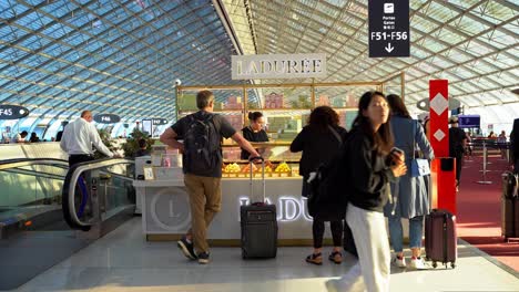 Ladurée-Luxus-Reposterie-Laden-Am-Pariser-Flughafen,-Kiosk-Mit-Symmetrischer-Decke,-Touristen-Mit-Gepäck