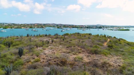 Drone-flies-over-arid-coastal-desert-to-yachts-anchored-in-Spanish-Waters,-Curacao
