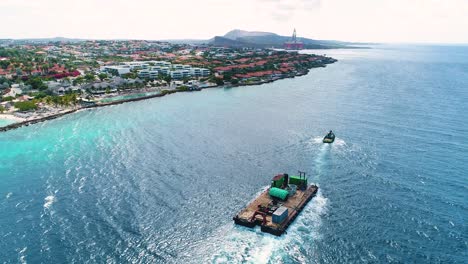 Tug-boat-pulls-barge-along-Caribbean-island-coastline-at-midday-in-beautiful-blue-ocean-water