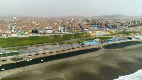 Aerial-view-tilting-toward-the-coastline-of-sunny-Huacho-city,-hazy-day-in-Peru