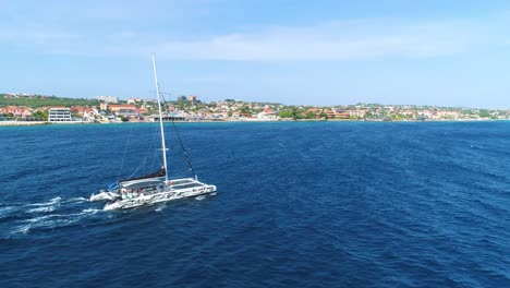 Bluefin-catamaran-cruises-along-vibrant-blue-Caribbean-ocean-water-against-current,-aerial-tracking