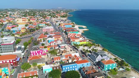 Aerial-reverse-dolly-above-Pietermaai,-Punda,-and-Willemstad-vibrant-buildings-of-Curacao-with-incredible-blue-ocean-water