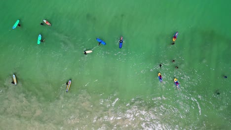 Aerial-of-surfers-with-colorful-surfboards-in-the-green-ocean-of-Selong-Belanak-Beach,-Indonesia