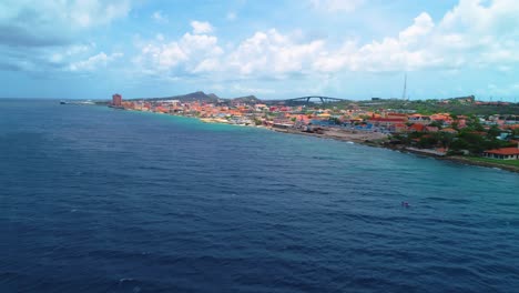 Aerial-dolly-above-ocean-waters-of-Curacao,-flyover-to-Willemstad-and-Pietermaai-neighborhoods