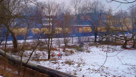 People-walk-in-desolate-and-industrial-landscape-while-cargo-train-with-chemicals-passes-by