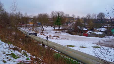 Man-walking-through-desolate-snowy-industrial-landscape-with-houses-and-pipeline