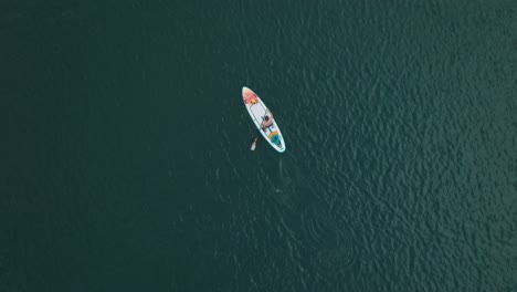 Hombre-Remando-En-Tabla-De-SUP-Sobre-Un-Lago-De-Aguas-Azules-Profundas