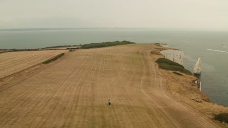 Cyclist-rides-towards-White-Cliffs-of-Dover-in-Britain,-UK-while-Drone-ascends-slowly