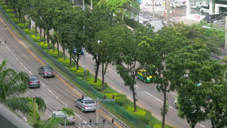 View-from-the-top-of-a-street-in-the-city,-with-cars-and-public-transport-passing-by-in-Bangkok,-Thailand