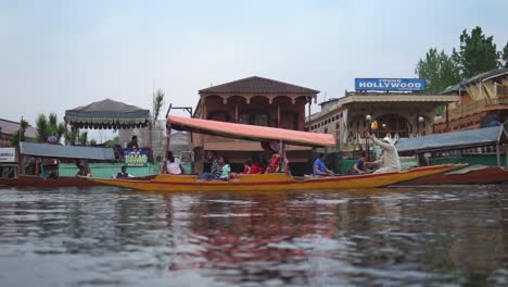 Man-rowing-a-shikara-through-the-dal-lake-in-Srinagar,-Kashmir,-India-with-passengers-onboard