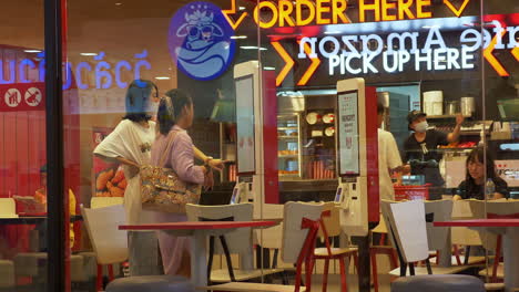 Zooming-out-of-the-customers-inside-KFC-or-Kentucky-Fried-Chicken-restaurant-who-are-using-a-digital-menu-board-in-ordering,-while-some-are-already-eating-their-meals
