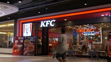 Alejándose-De-La-Sucursal-De-Comida-Rápida-De-Kfc-O-Pollo-Frito-De-Kentucky-Dentro-De-Un-Centro-Comercial-En-Bangkok,-Tailandia,-Donde-Los-Clientes-Piden-Comida-Y-Otros-Disfrutan-De-Una-Comida-Rápida