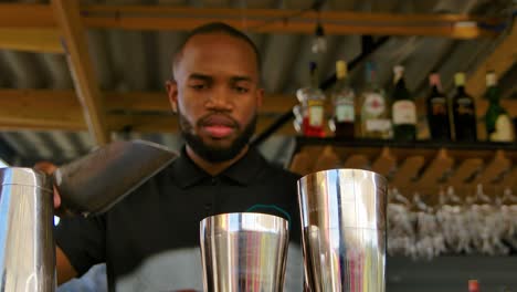 Handsome-young-black-man-pours-ice-into-stainless-steel-shakers-at-bar