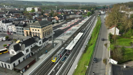 Aerial-flyover-train-station-with-arriving-train-with-passenger-in-Wavre,-Belgium