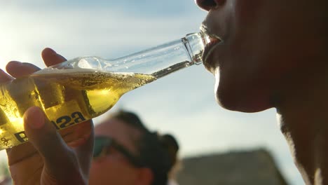 Freund-Hebt-Eine-Glasflasche-Bier-In-Den-Mund,-Nippt-Und-Trinkt-Und-Entspannt-Sich-Bei-Sonnenuntergang-Mit-Freunden