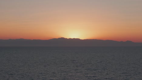 Warmer,-Leuchtend-Orangefarbener-Sonnenuntergang,-Der-Hinter-Dem-Wolkigen-Horizont-über-Dem-Ruhigen-Mittelmeer-Verblasst
