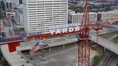 Aerial-orbiting-shot-showing-construction-site-crane-in-Atlanta-city-with-waving-american-flag