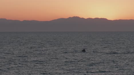 Aerial-view-overlooking-sailing-boat-navigating-Mediterranean-sea-with-glowing-Turkish-sunset-horizon
