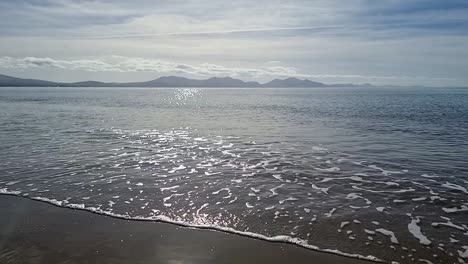 Hazy-Snowdonia-mountain-range-across-idyllic-shimmering-Irish-Seascape-in-slow-motion-from-Newborough-beach-shoreline
