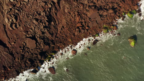 Top-Down-aerial-drone-shot-of-red-rocky-volcanic-coastline