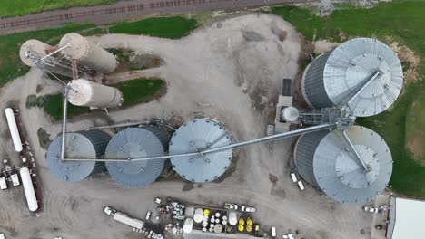 Top-down-aerial-shot-of-industrial-silos-and-storage-tanks-with-connecting-machinery-on-a-gravel-site