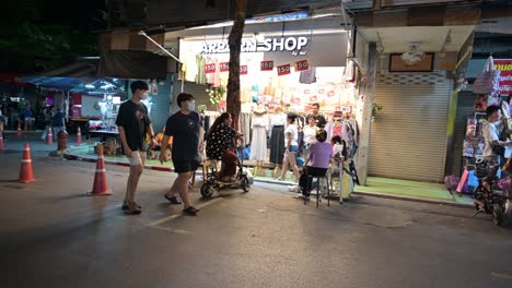 Zwei-Männliche-Personen-In-Schwarz-Mit-Masken-Und-Dann-Eine-Familie,-Die-über-Den-Berühmten-Chatuchak-Wochenendmarkt-In-Bangkok,-Thailand,-Spaziert
