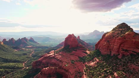 Sun-pierces-clouds-behind-red-rock-valley-of-Merry-Go-Round-Sedona-Arizona,-aerial-panoramic-overview