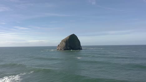 Drone-flying-low-over-water-straight-towards-Haystack-Rock-in-Pacific-City,-Oregon-Coast