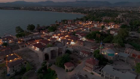 Aerial-view-over-illuminated-Side-old-town-traditional-Turkish-suburban-neighbourhood-homes-after-sunset